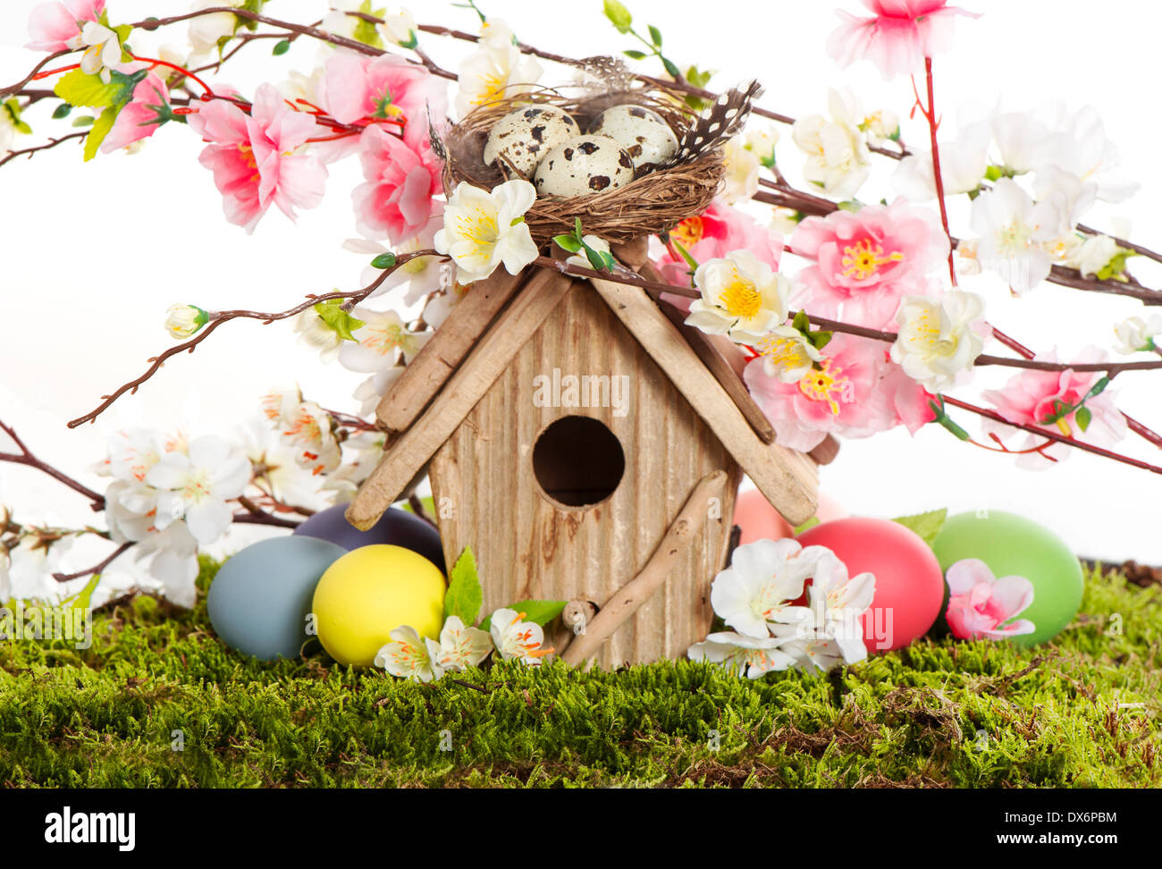 colorful easter decoration with birdhouse and eggs on green grass. spring apple and cherry blossoming Stock Photo
