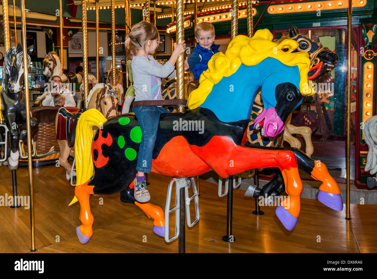 Young riders on carousel horses at Carousel for Missoula amusement park in Missoula, Montana, USA Stock Photo