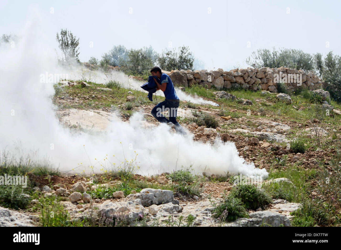 Hebron, West Bank. 19th Mar, 2014. Palestinian protester runs to take cover of gas fired by Israeli soldiers during clashes after Palestinian teenager Yussef Shawamreh was killed, near security fence in the West Bank city of Hebron on March 19, 2014. Shawamreh, 16 years old, was shot near the Palestinian village of al-Ramadin, south of Hebron, when he and three of his friends were attempting to cross the separation fence between Israel and the Palestinian territories. Credit:  Mamoun Wazwaz/Xinhua/Alamy Live News Stock Photo