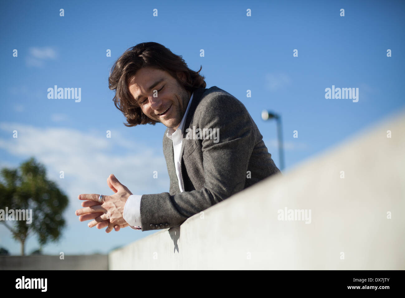 A young male model leaning against a wall with a blue sky behind him Stock Photo