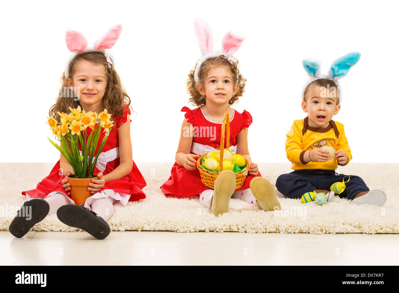 Happy three brothers sitting in a line on carpet and holding Easter eggs and flowers Stock Photo