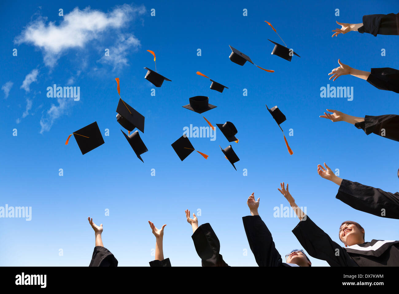 Students throwing graduation hats in the air celebrating with blue sky Stock Photo