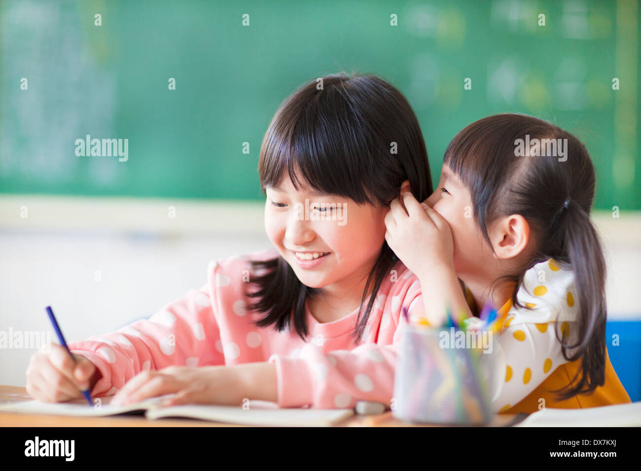 Two young girls whispering and sharing a secret in the classroom Stock Photo