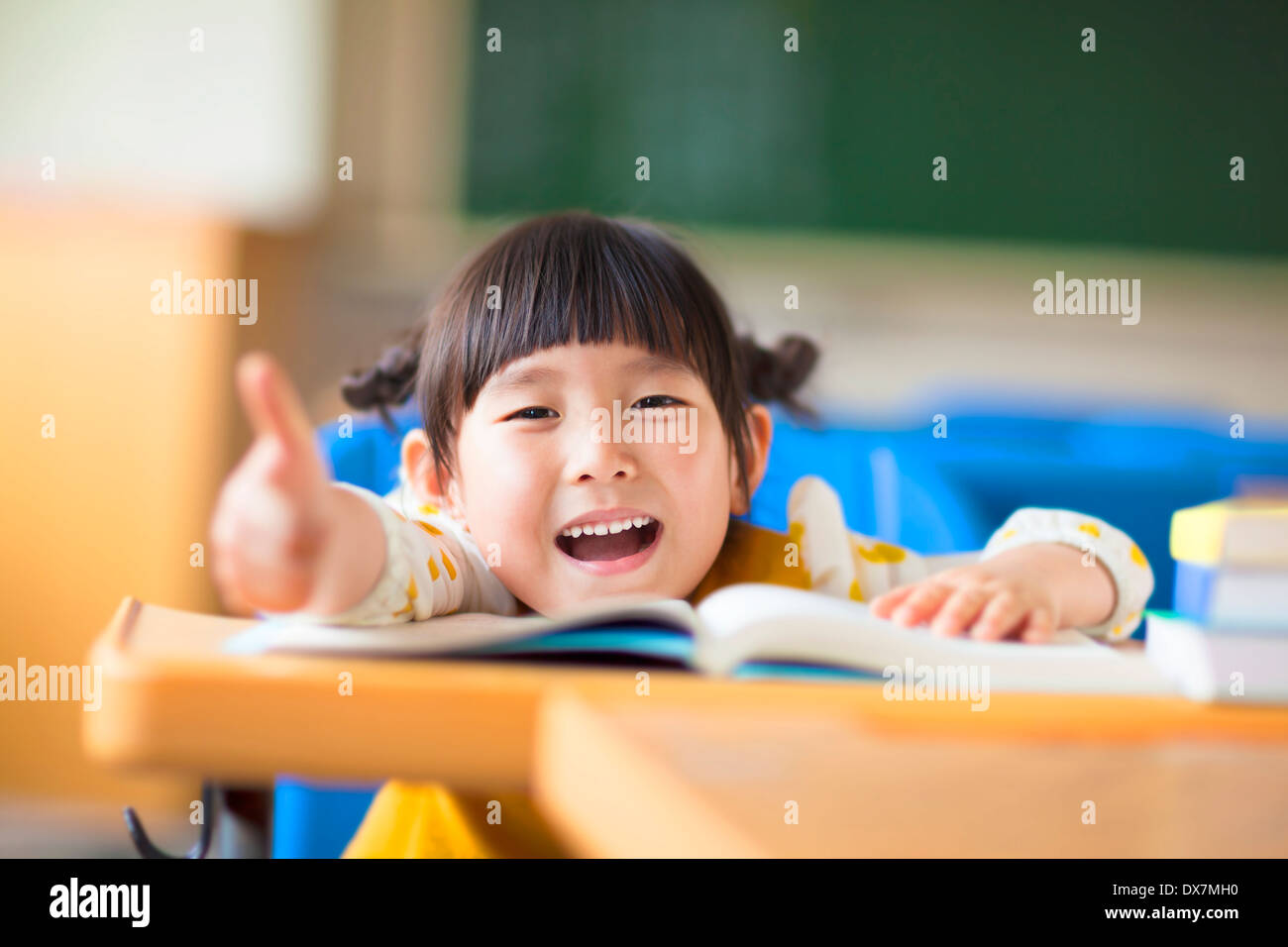happy kid thumb up with book in a classroom Stock Photo