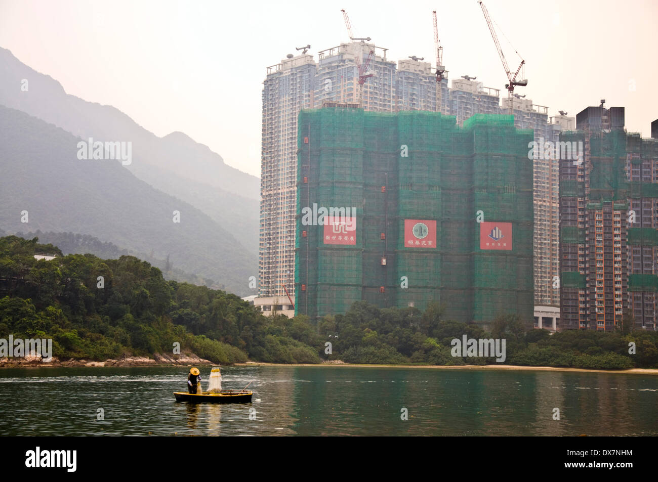 Starfish Bay, Ma On Shan, New Territories, Hong Kong. 20th March, 2014.  A subsistence fisherman brings in his net in the shadow of Double Cove luxury apartments construction behind him. Phase one of the development consists of 928 flats however analysts forecast a 10 percent drop in property prices this year as tax increases and rising borrowing costs cool demand. Credit:  Richard Wayman/Alamy Live News Stock Photo