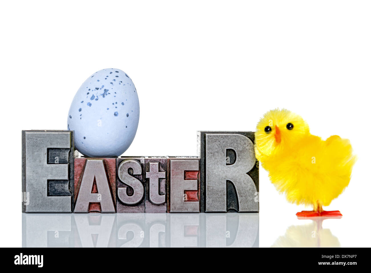 The word Easter in old metal letterpress with a toy chick and candy covered chocolate egg, isolated on a white background. Stock Photo