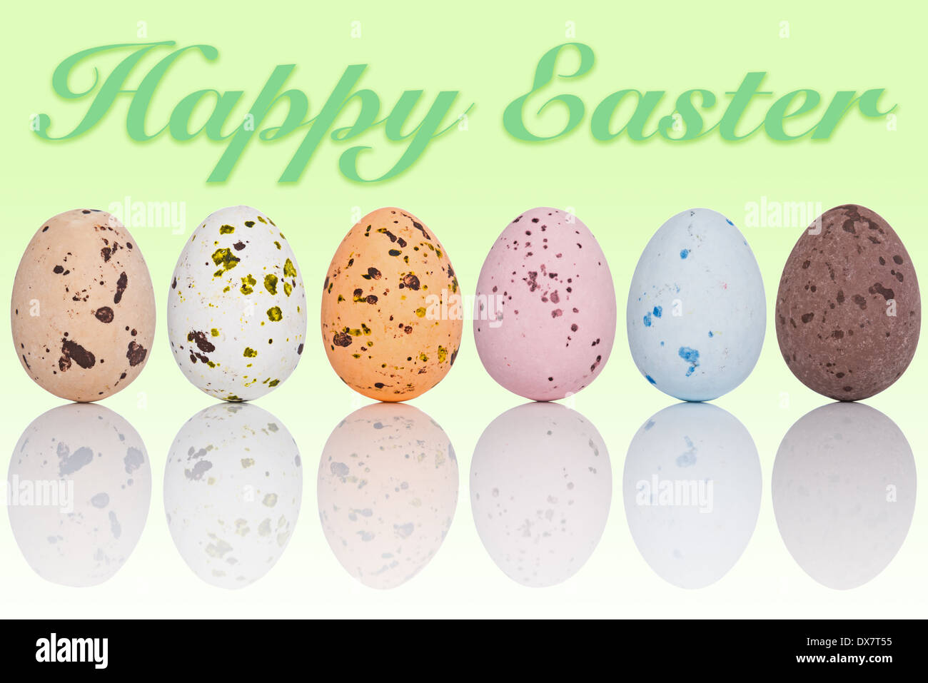 Six candy coated chocolate Easter eggs in a line, with the text Happy Easter on a graduated background. Stock Photo