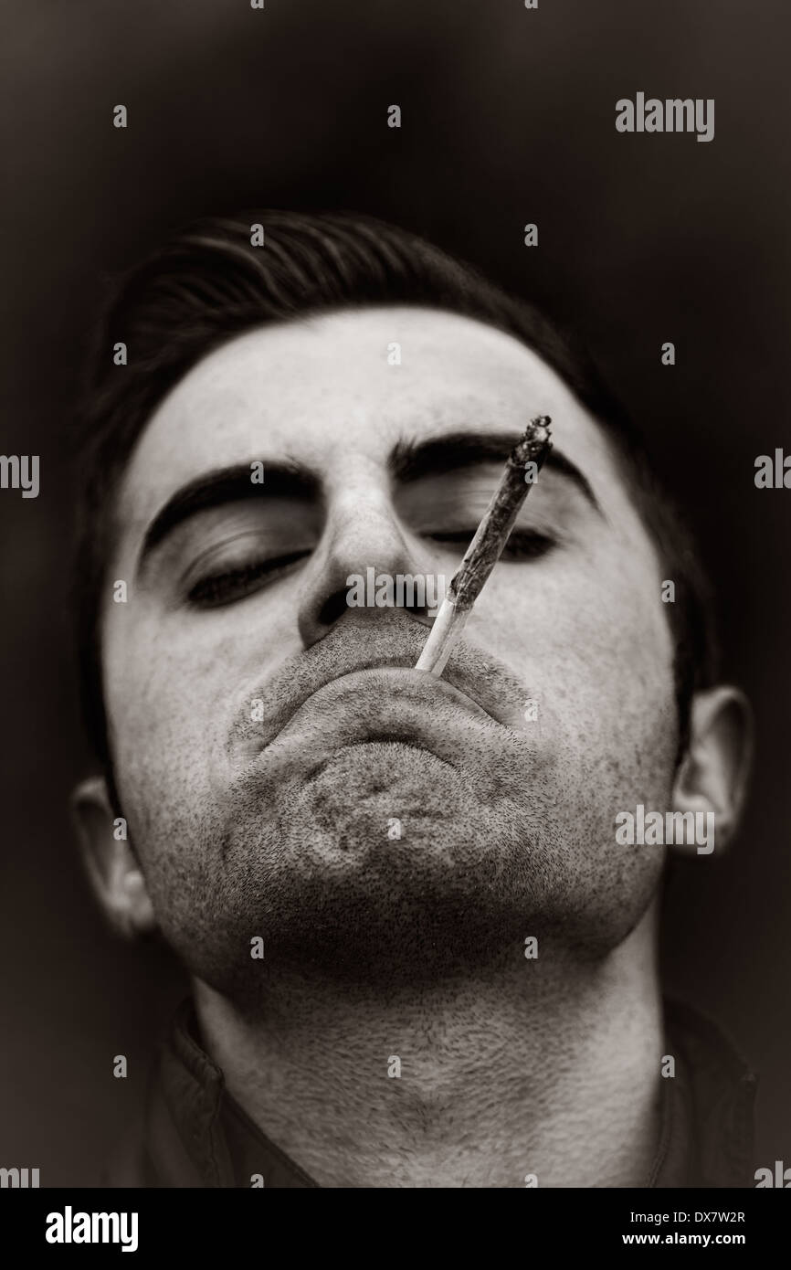 Black and white portrait of young man with closed eyes enjoying his marijuana or joint Stock Photo