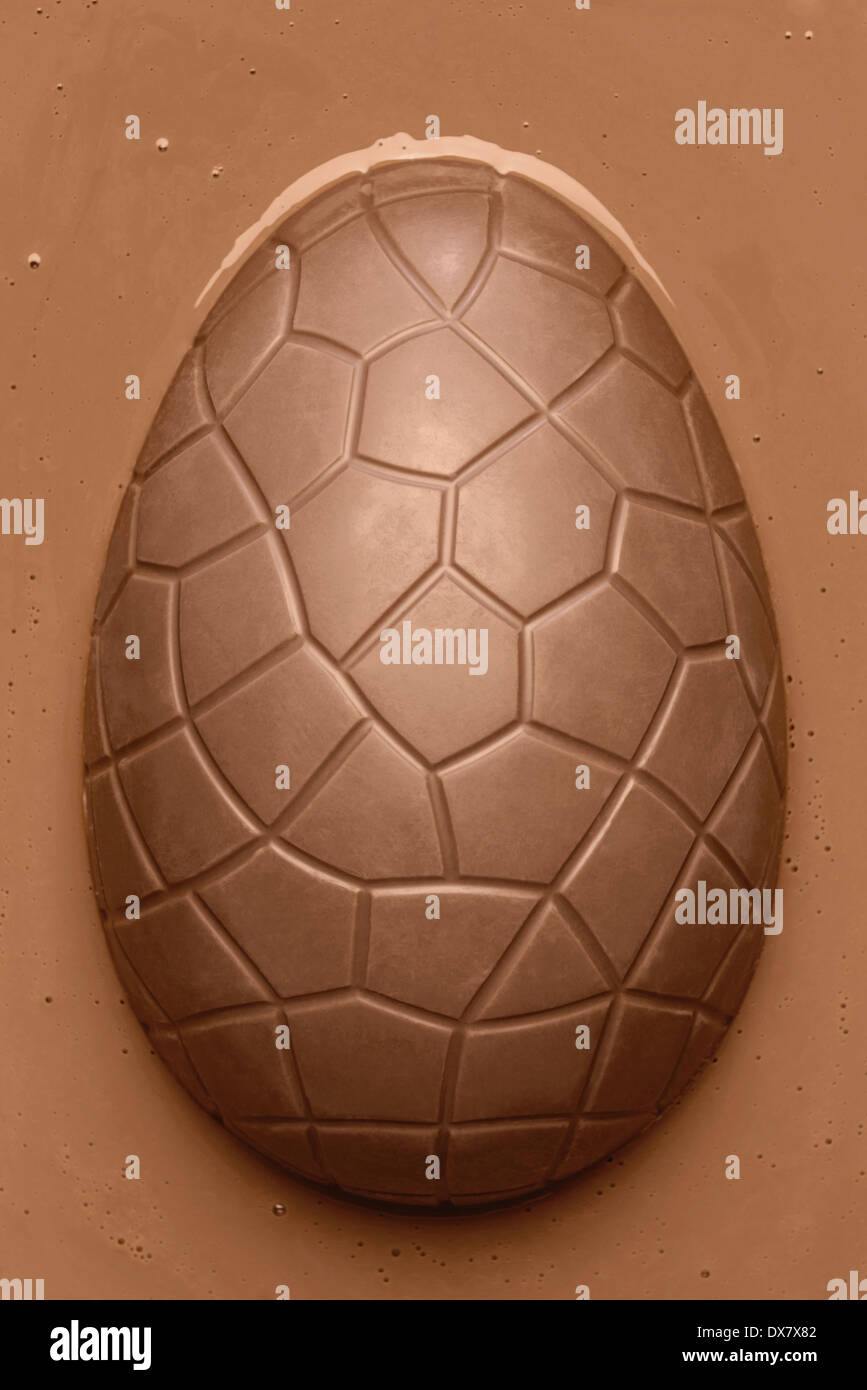 Chocolate Easter egg emerging from smooth melted milk chocolate Stock Photo