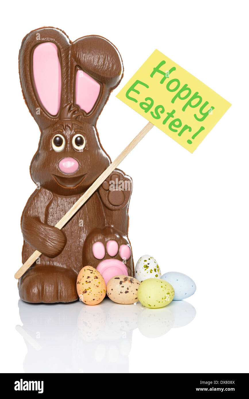 Chocolate bunny holding a sign that says Hoppy Easter, with some candy eggs at his feet. Isolated on a white background. Stock Photo