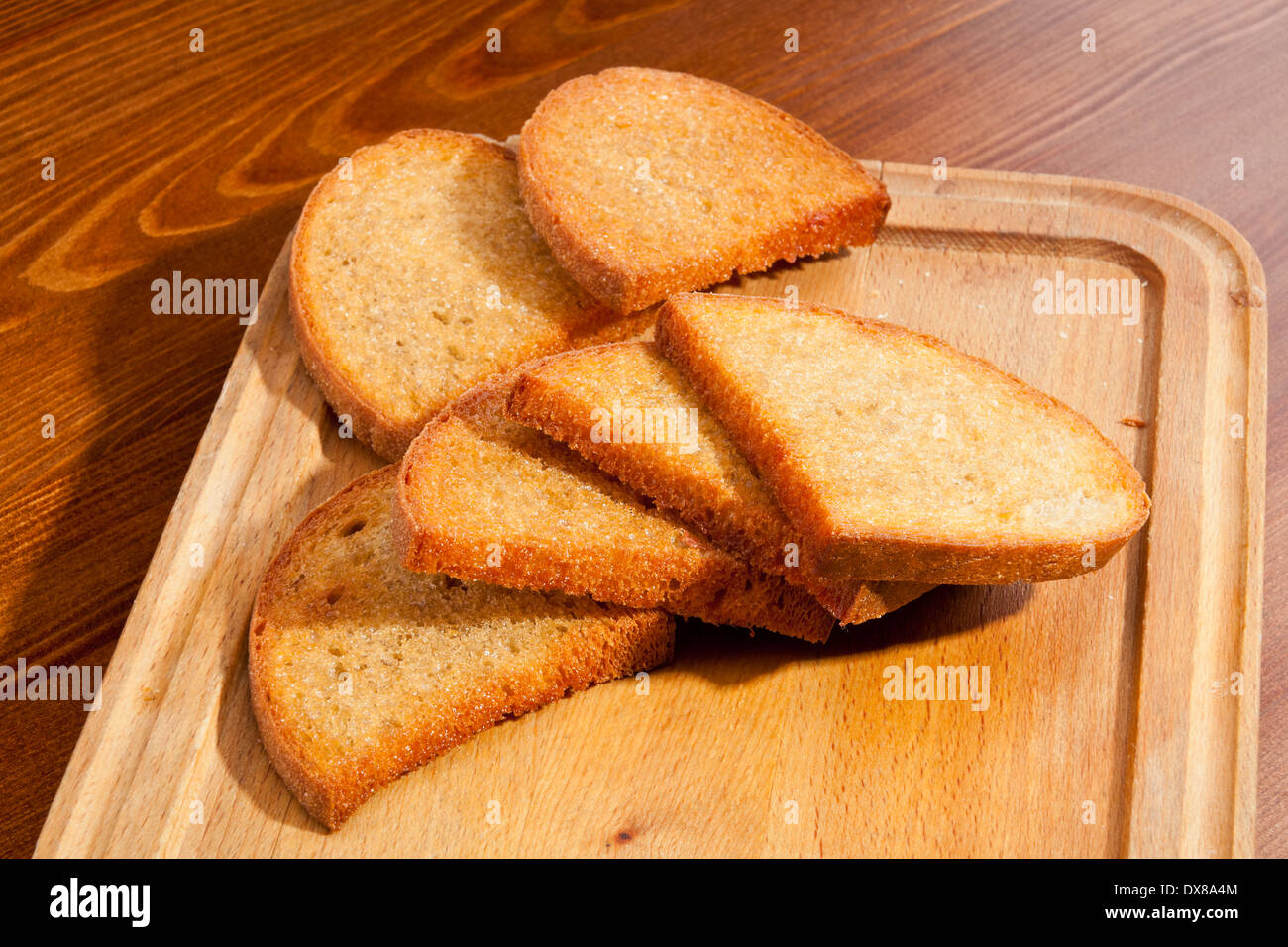Crusty toasts on wooden trencher Stock Photo