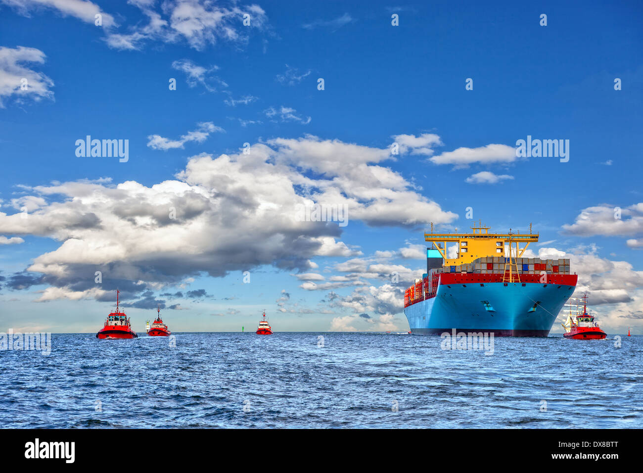 Tugboat assisting container cargo ship to harbor. Stock Photo