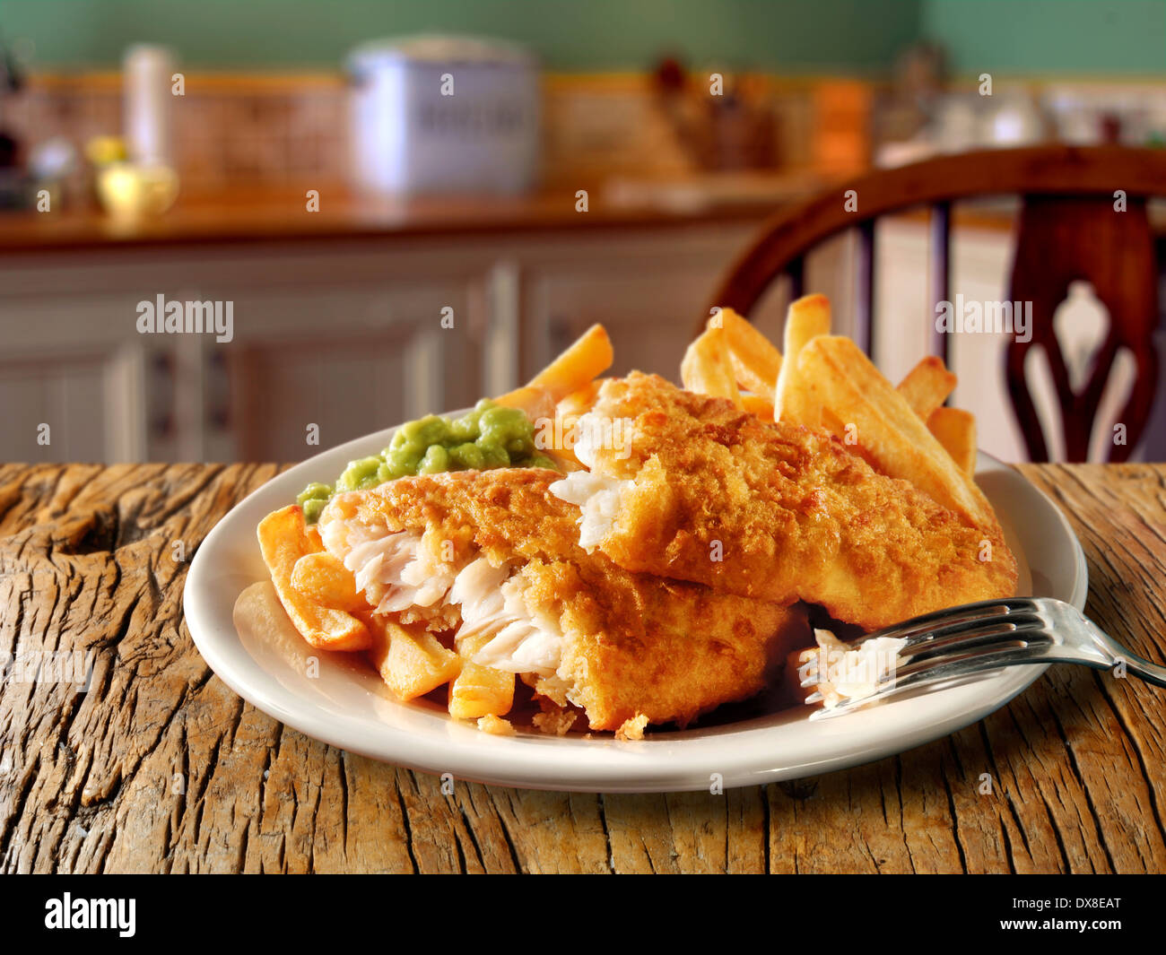 Traditional British  Battered Fish And Chips served on a plate in a traditional kitchen setting ready to eat Stock Photo