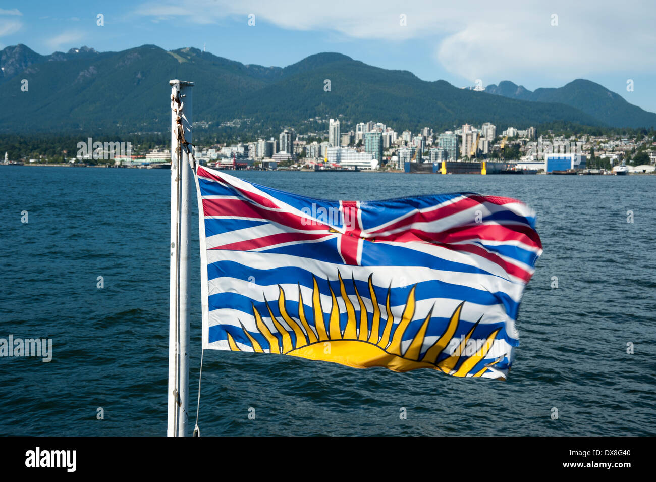 British Columbia flag with the city of North Vancouver and mountains in the background across the water of Georgia Strait Stock Photo