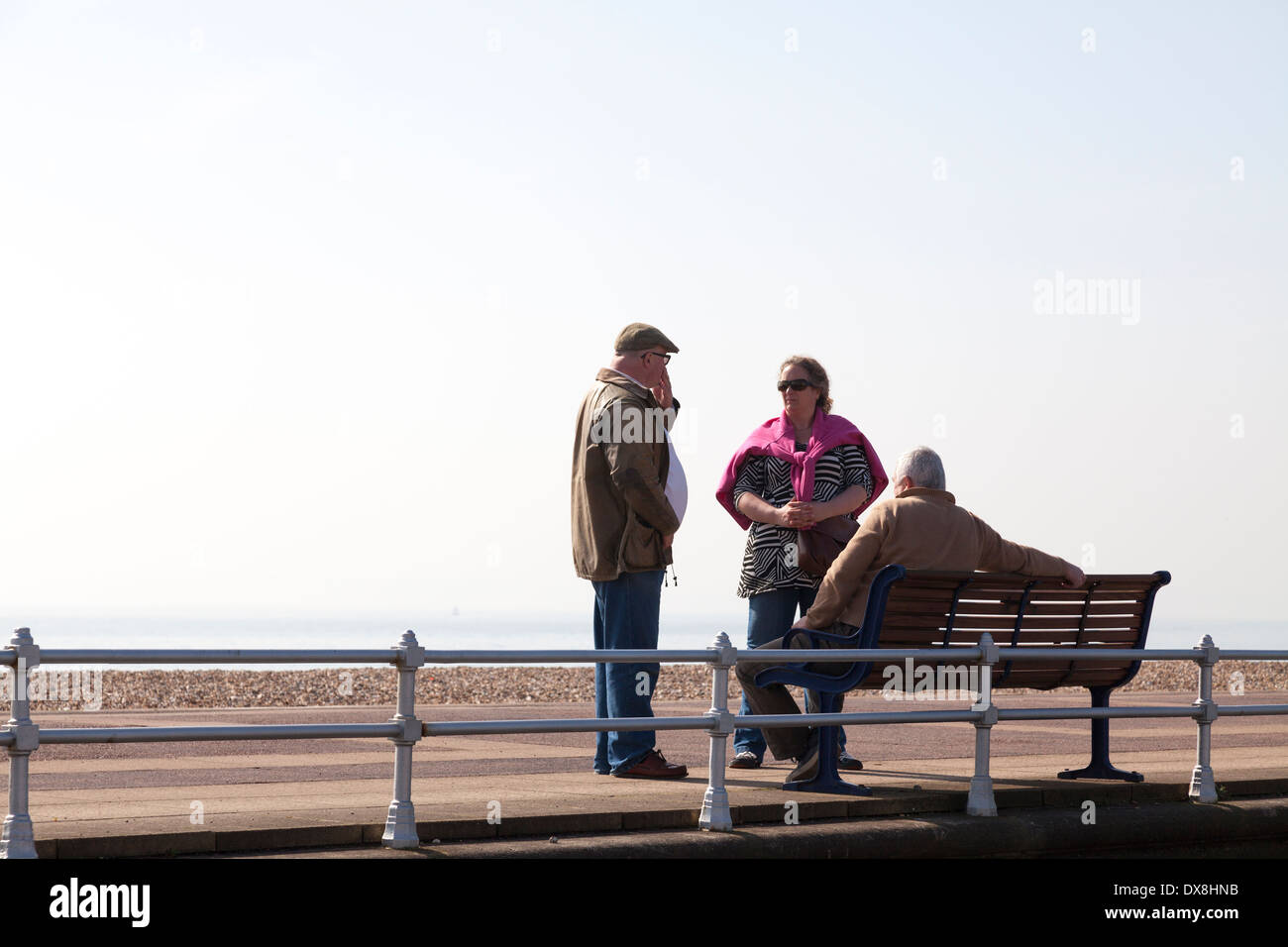 Middle aged group of three friends around bench on promenade. Stock Photo