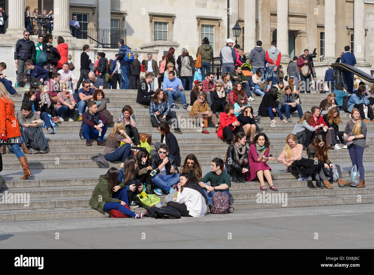 Tourists sitting on the steps in Trafalgar Square near the National Gallery, London, England, United Kingdom. Stock Photo
