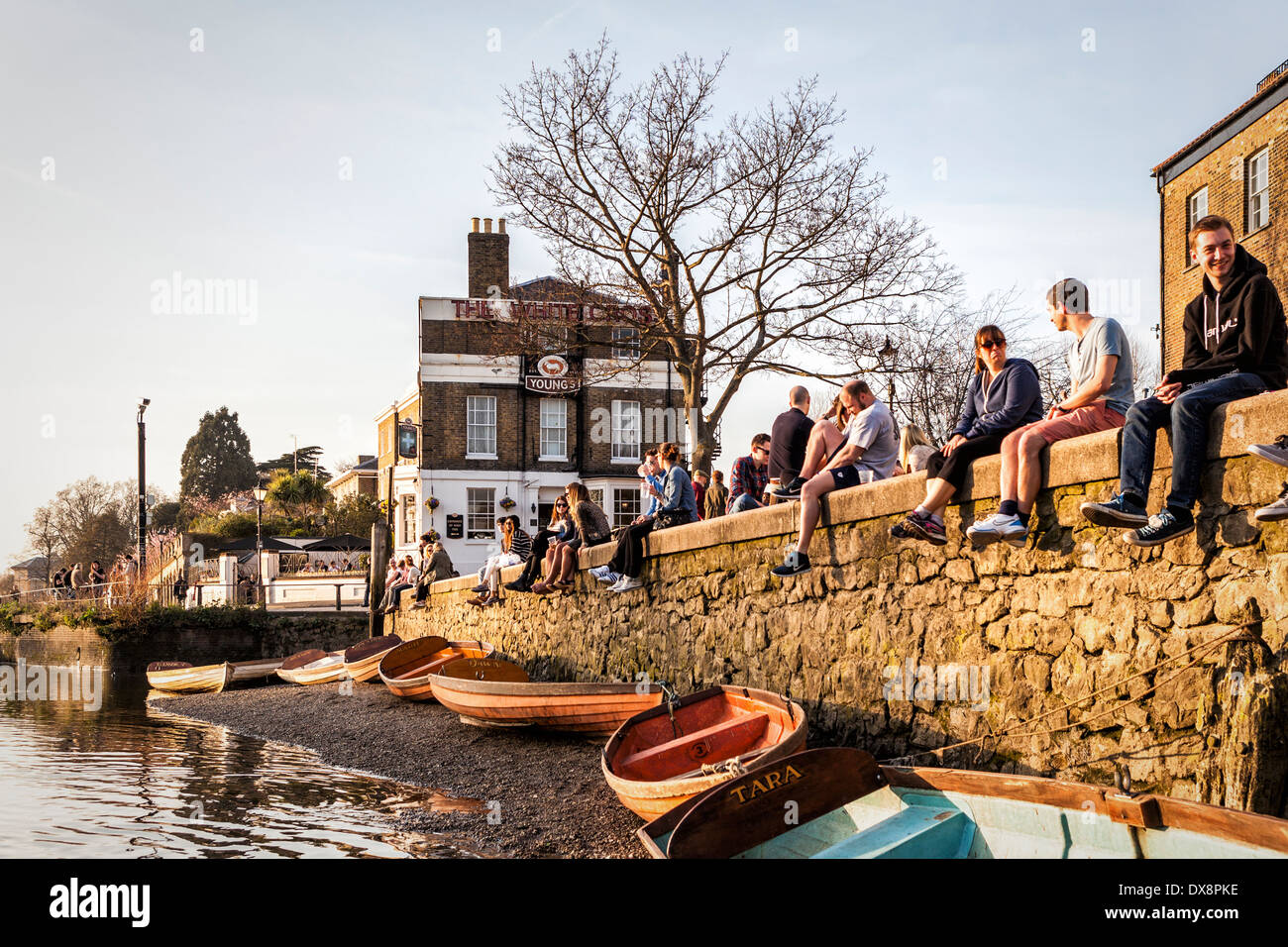 People sitting on banks of the river Thames near the White Cross pub in warm Spring sunshine, Richmond upon Thames, London, UK Stock Photo