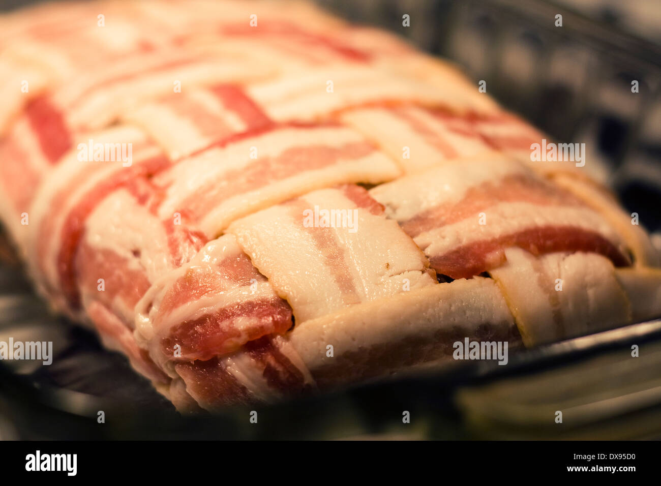 Close up of an uncooked Meatloaf wrapped with bacon in a basket weave