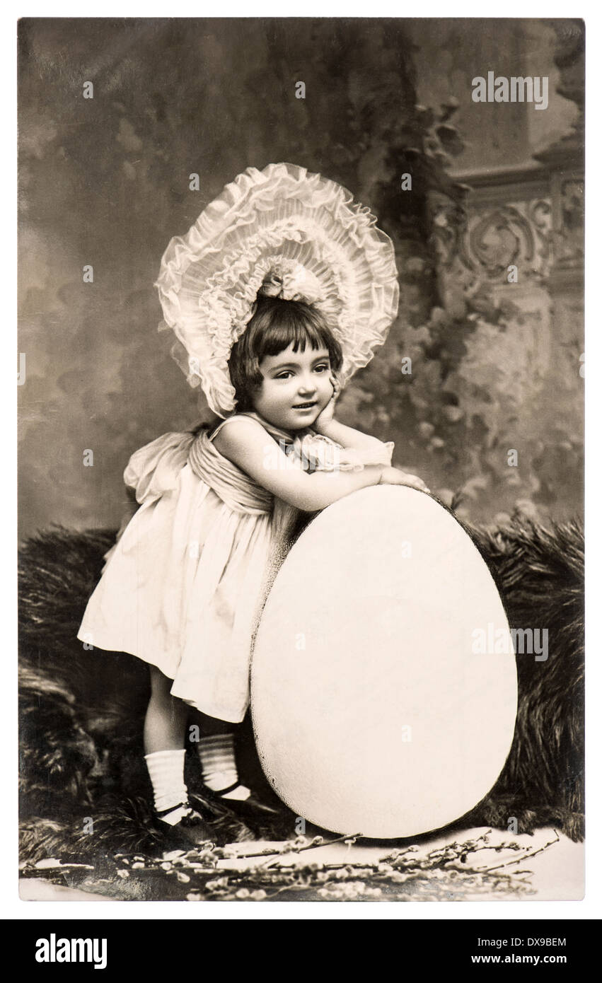 vintage easter card with funny sweet little girl and big egg. sentimental nostalgic background. antique photo from 1908 Stock Photo