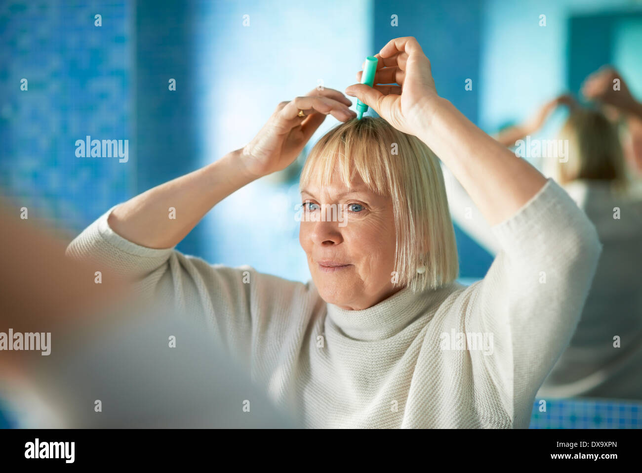 old caucasian woman applying lotion to prevent hair loss, looking at mirror in bathroom Stock Photo