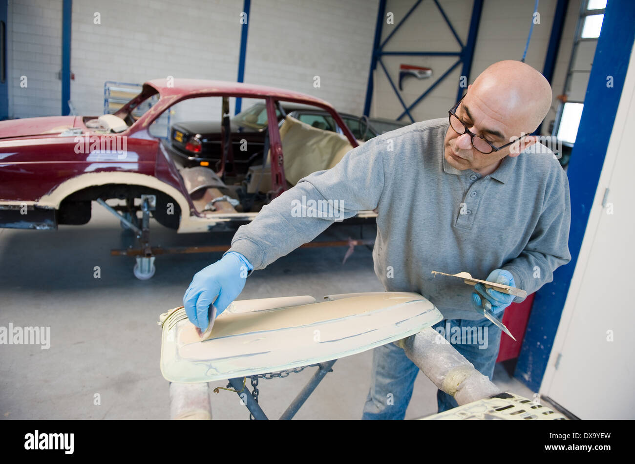 A car repairman is preparing a part of a car body for repainting in a garage Stock Photo