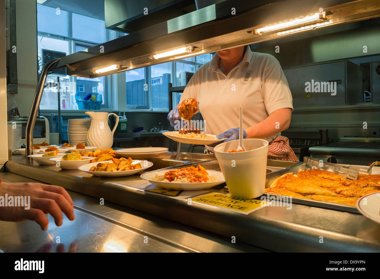 A woman at work dishing out serving food in a school canteen, Wales UK