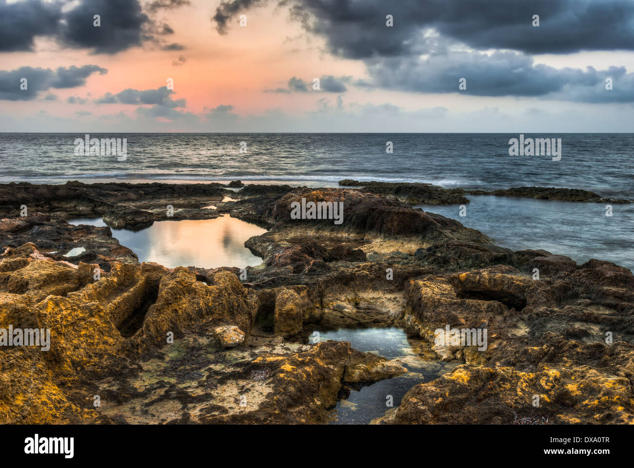 rocky beach with rock pools at sunset with cloudy sky Stock Photo - Alamy