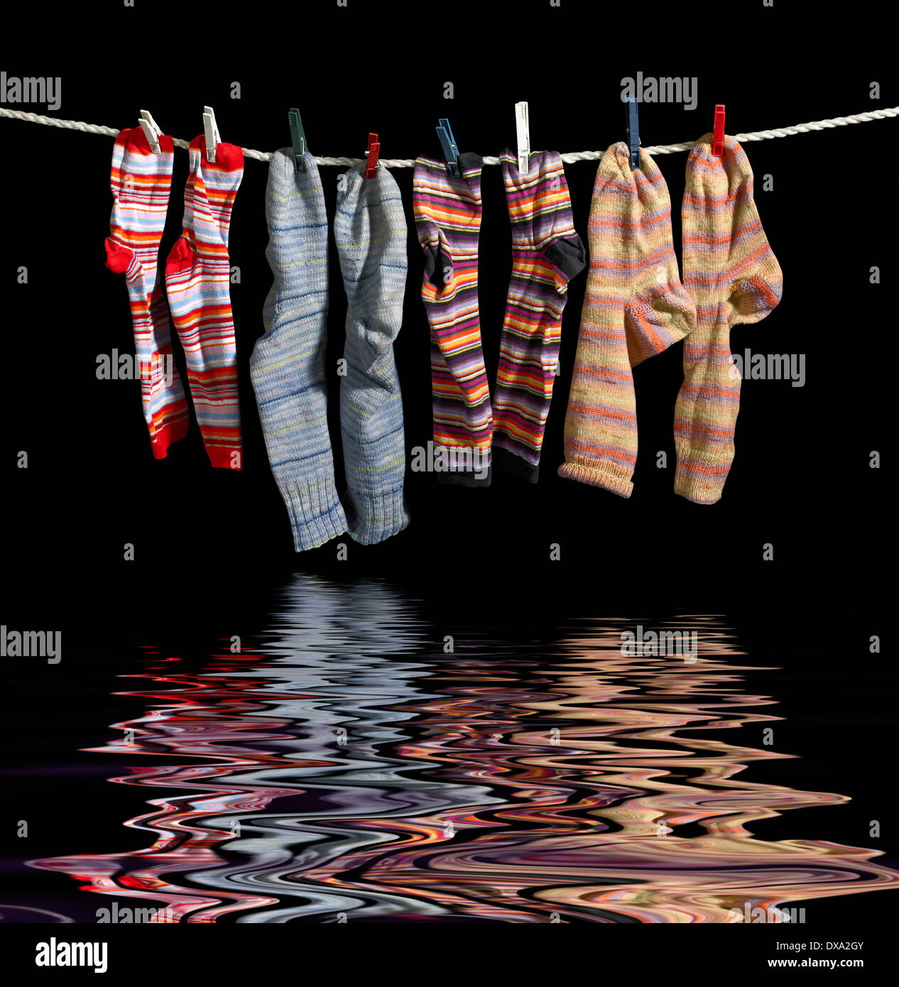 clothesline with some multicolored sox fixed with clothes pins over reflective water surface in black back Stock Photo