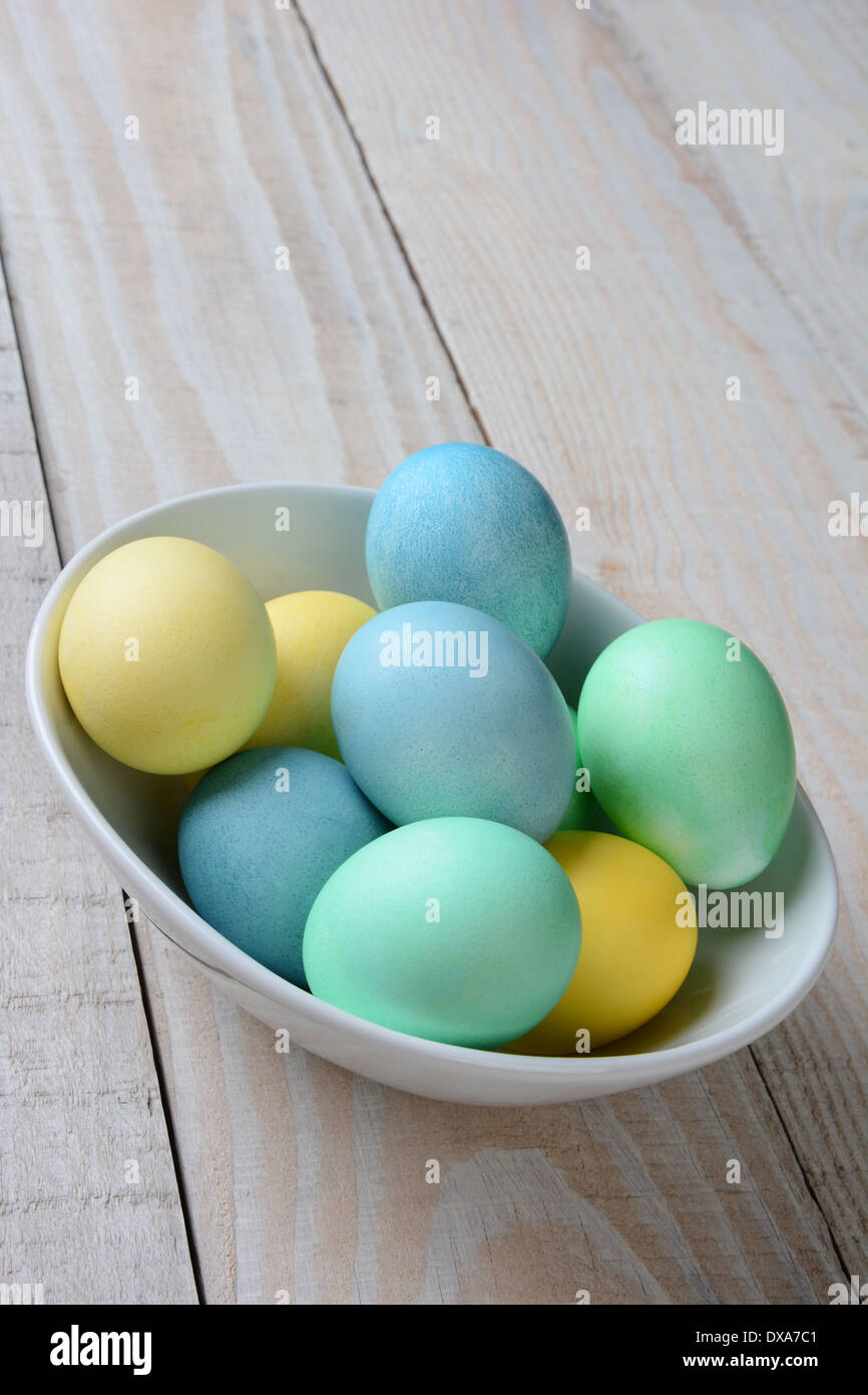Vertical high angle shot of a bowl of pastel Easter eggs. The white bowl is full of yellow, green and blue dyed eggs Stock Photo
