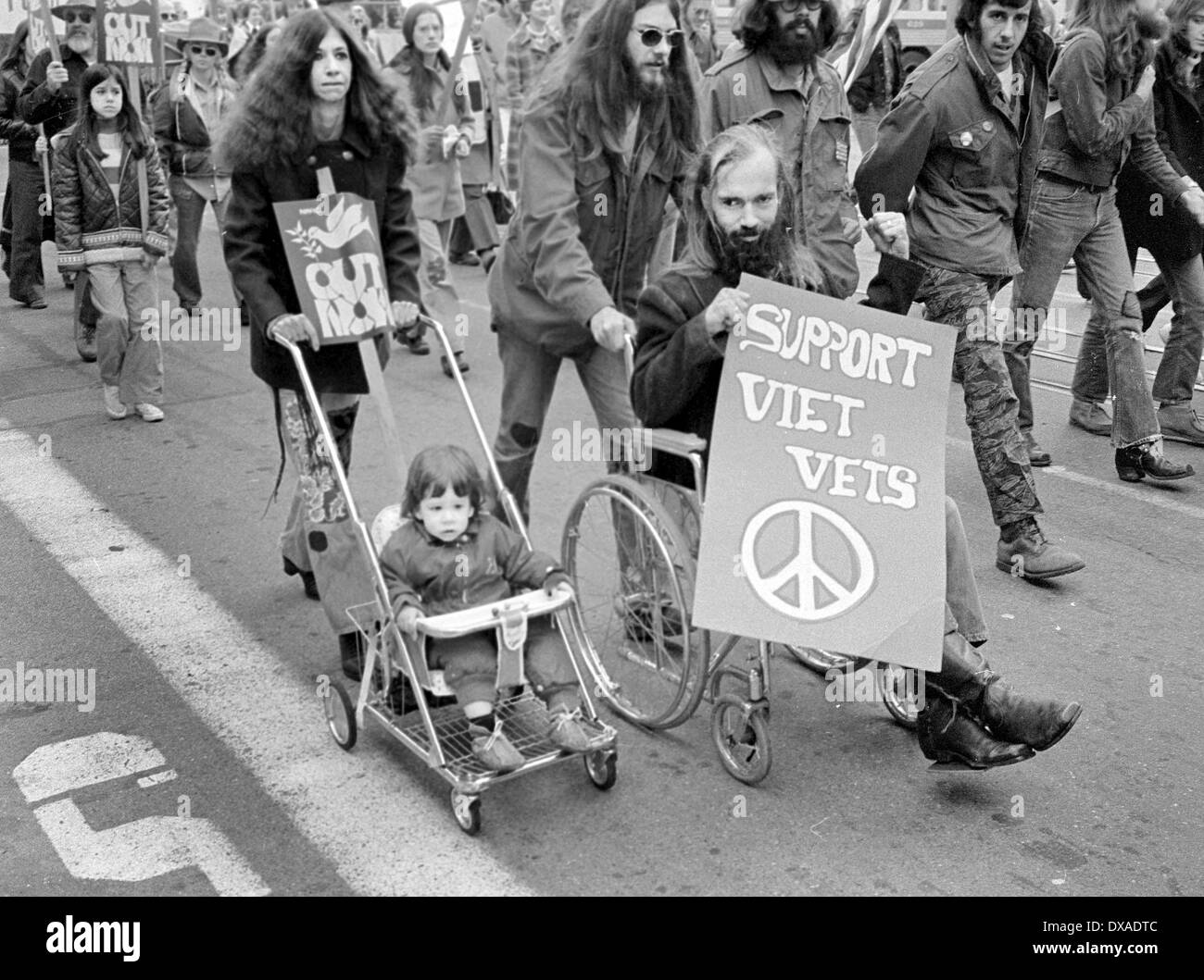 Contrast between a child too young to walk and anti-war protester pushed in wheel chair in San Francisco, Calif. in 1972 Stock Photo