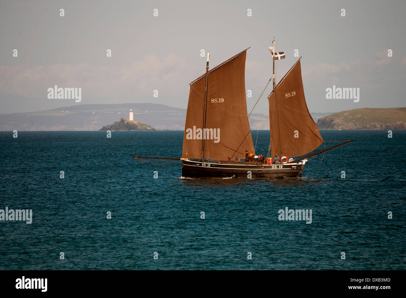 The ancient sailing lugger (a traditional fishing boat), the 'Ripple' in St Ives Bay, with Godrevy lighthouse, Cornwall, UK. Stock Photo