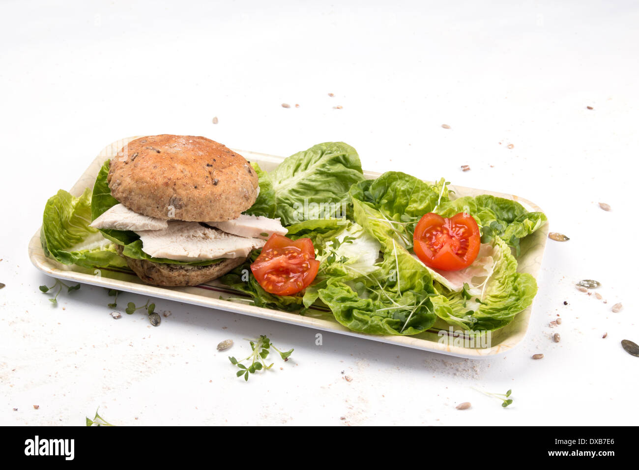 A chicken sandwich made with a seeded granary bread bun/cake/bap oblong white plate with tomato cress little Gem salad  (4of 5) Stock Photo
