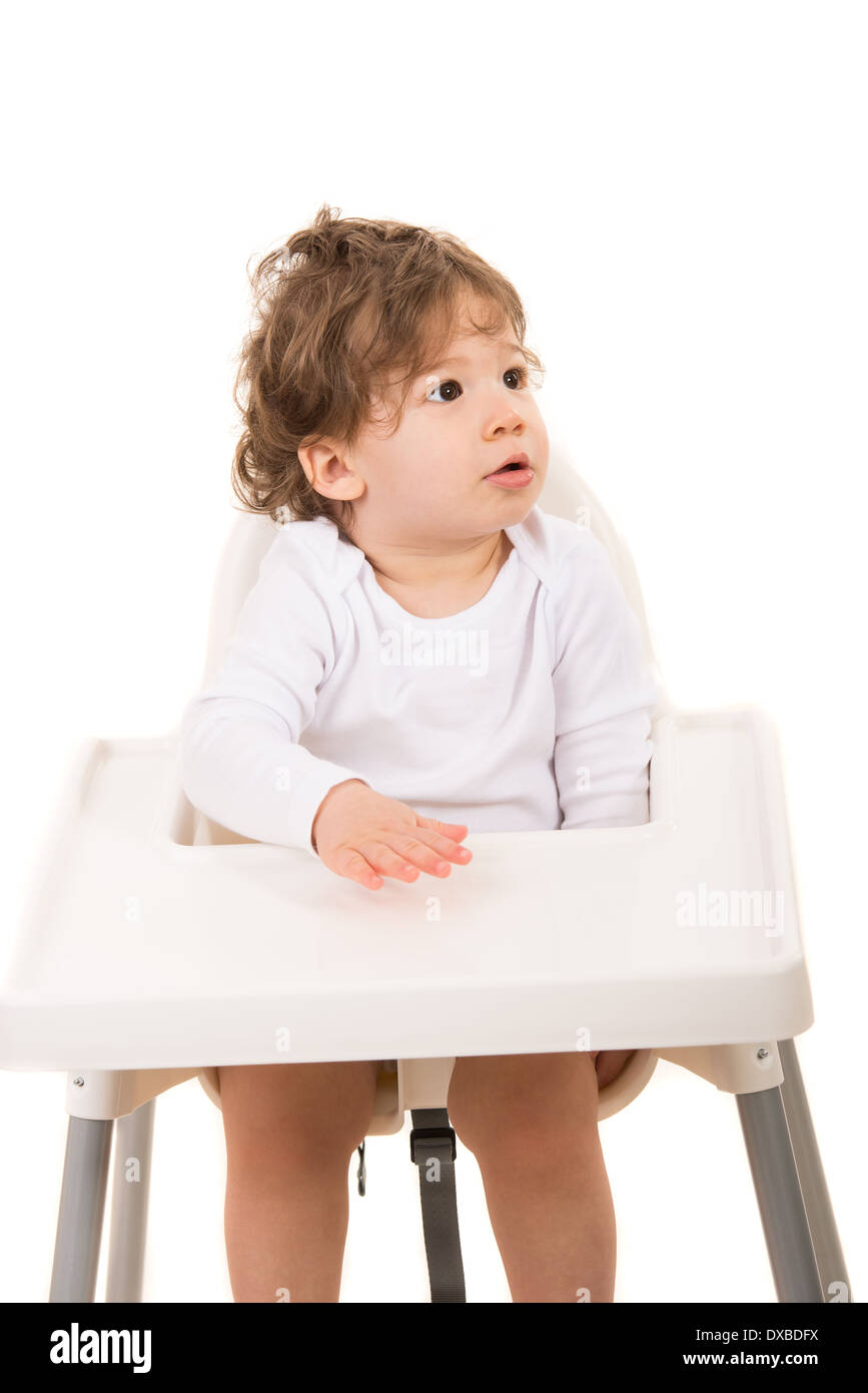 Toddler boy sitting in a high chair and looking away to copy space isolated on white background Stock Photo
