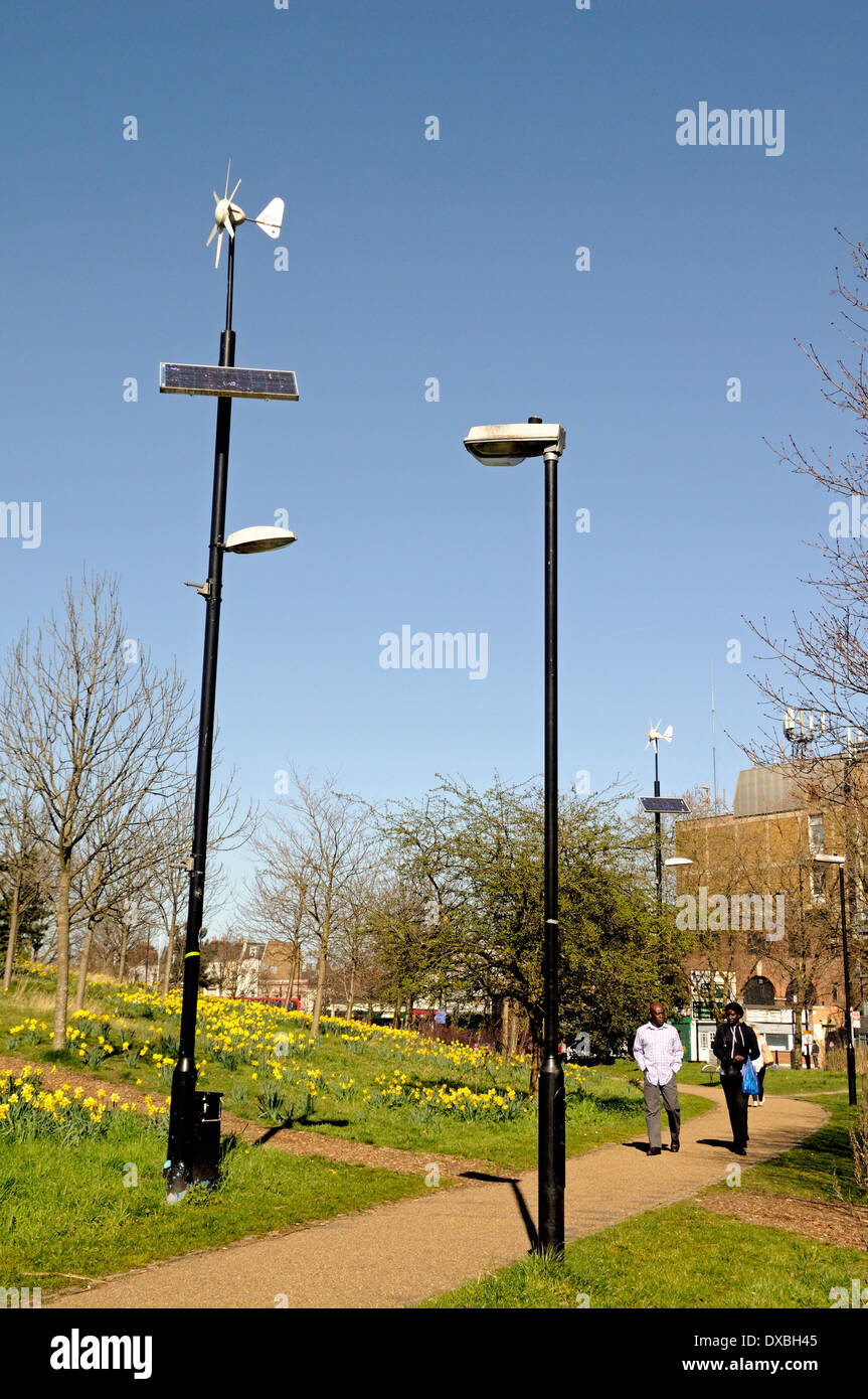 Wind and solar powered lamppost lamp post alongside conventional lamppost with people passing Mile End Park Tower Hamlets London Stock Photo
