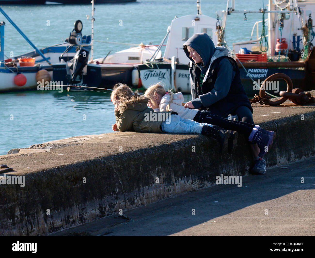 Mum and two daughters fishing from newlyn harbour wall, Penzance, Cornwall, UK Stock Photo