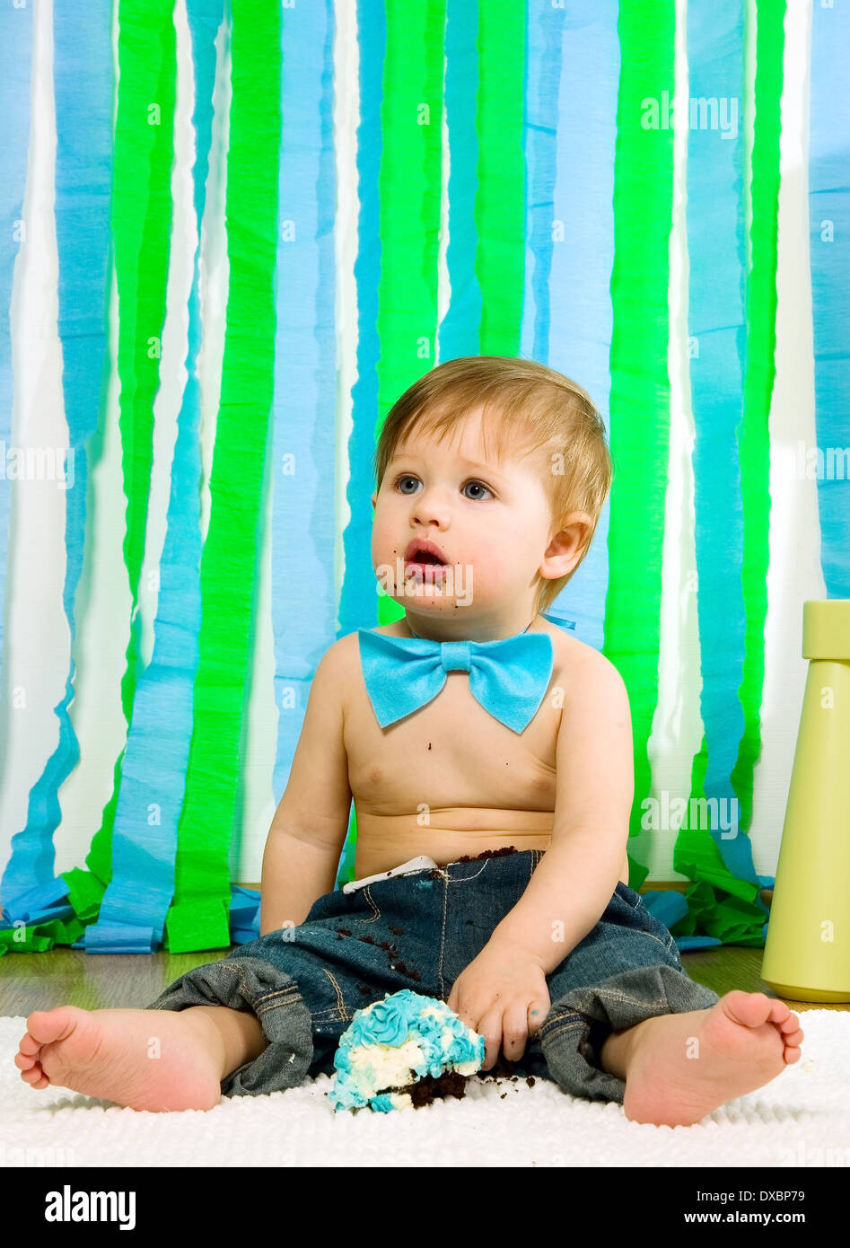 Child with blue bow-tie is celebrating his first birthday and eats cake Stock Photo