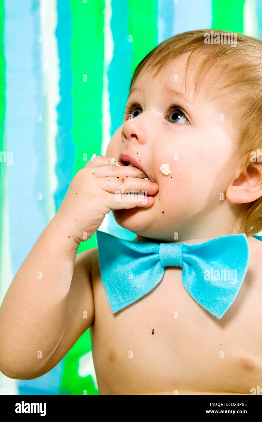 Child with blue bow-tie is celebrating his first birthday and eats cake Stock Photo