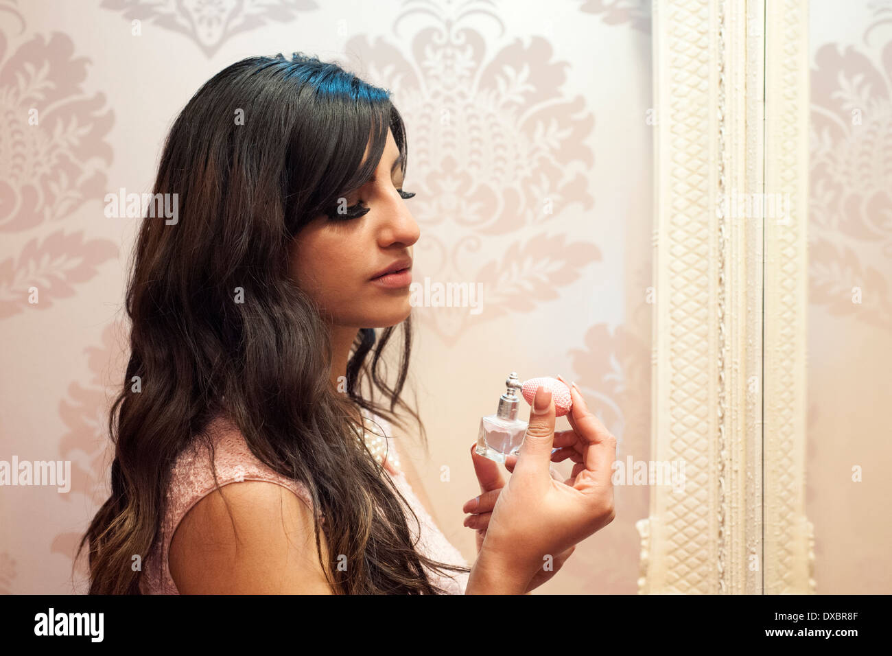 pretty young woman spraying herself with perfume from small bottle in front of large mirror Stock Photo