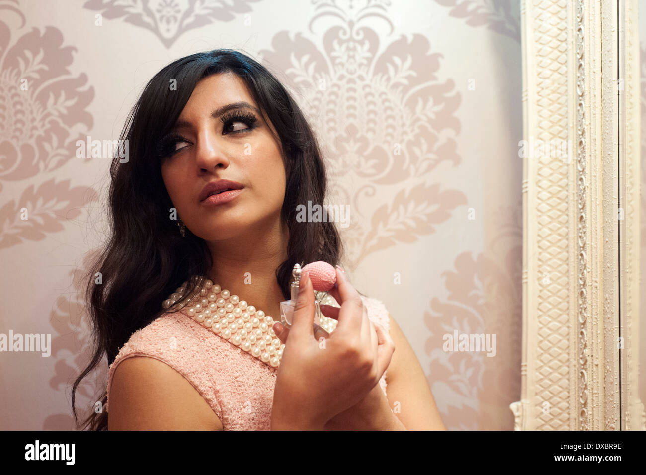 pretty young woman spraying herself with perfume from small bottle in front of large mirror Stock Photo