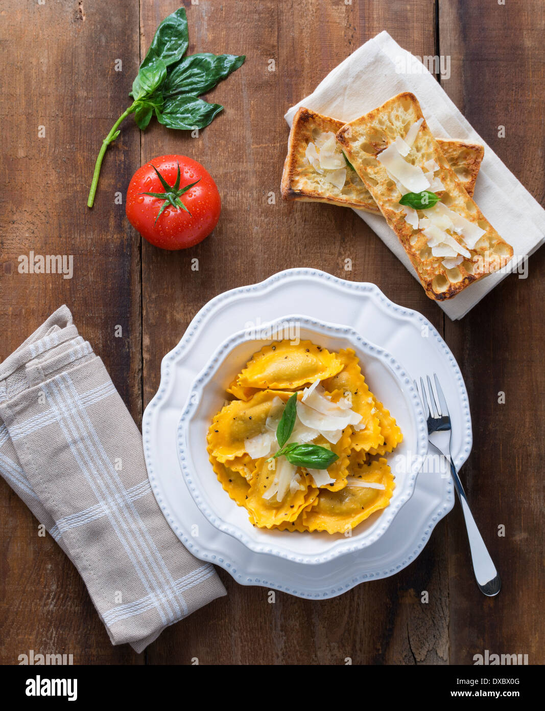 Butternut squash mezzaluna ravioli or tortellini with basil, tomato and crusting on rustic wood