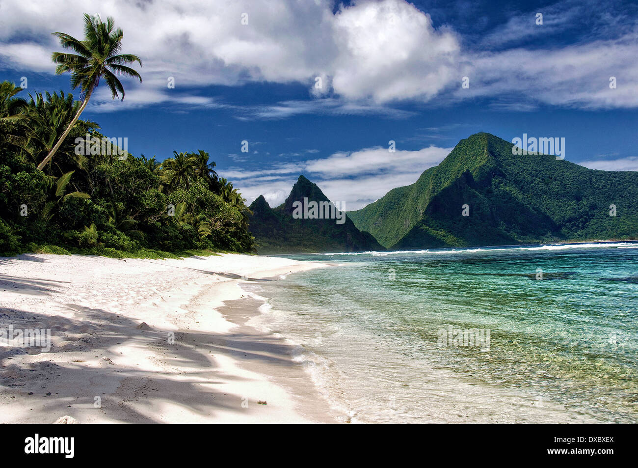 A secluded tropical sand beach and fringing reef in the Samoa National Park in Ofu Island, American Samoa. The island of Olosega rises in the distance. Stock Photo
