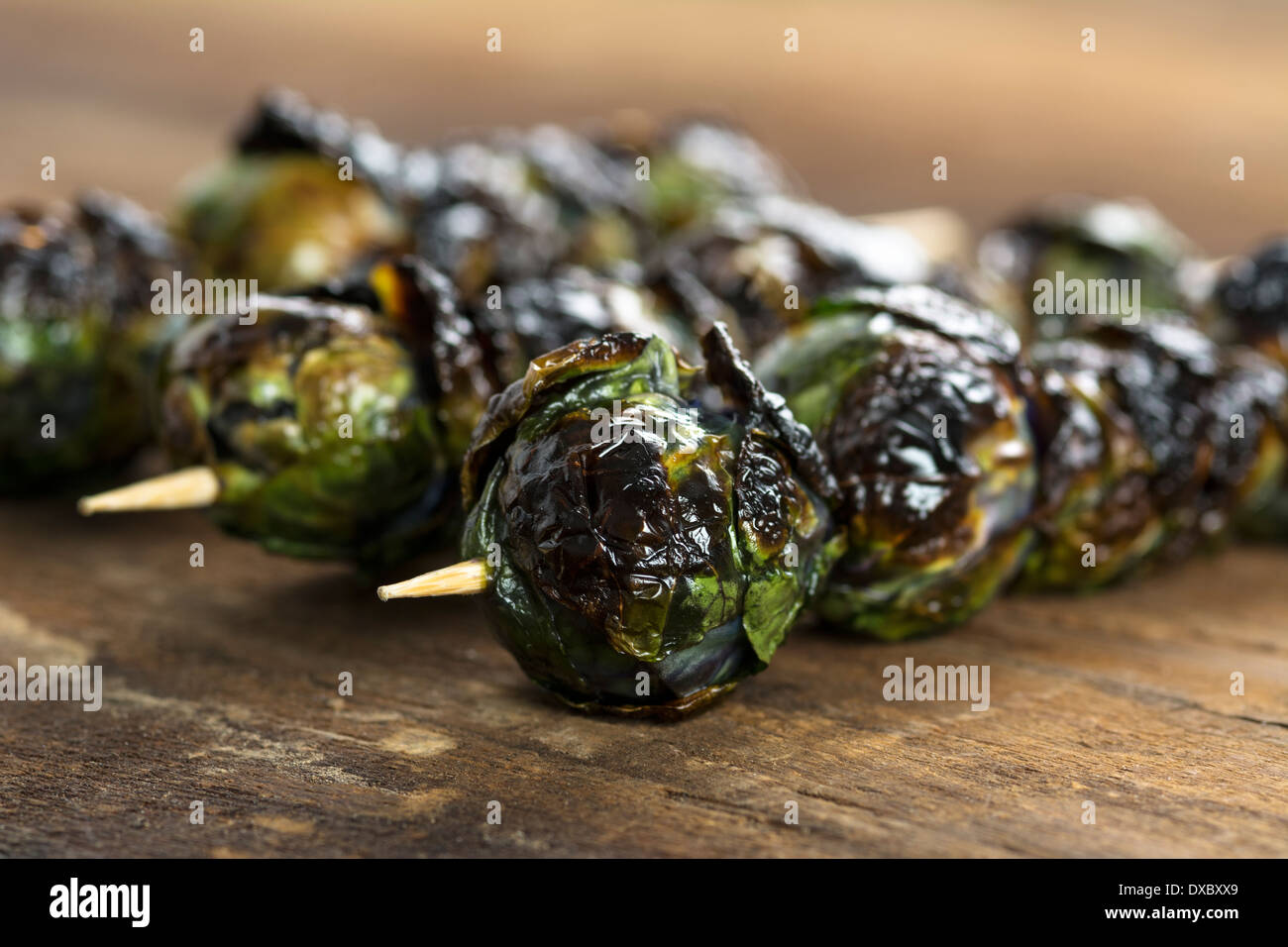 Three grilled organic purple Brussels spouts on skewers set on wood Stock Photo