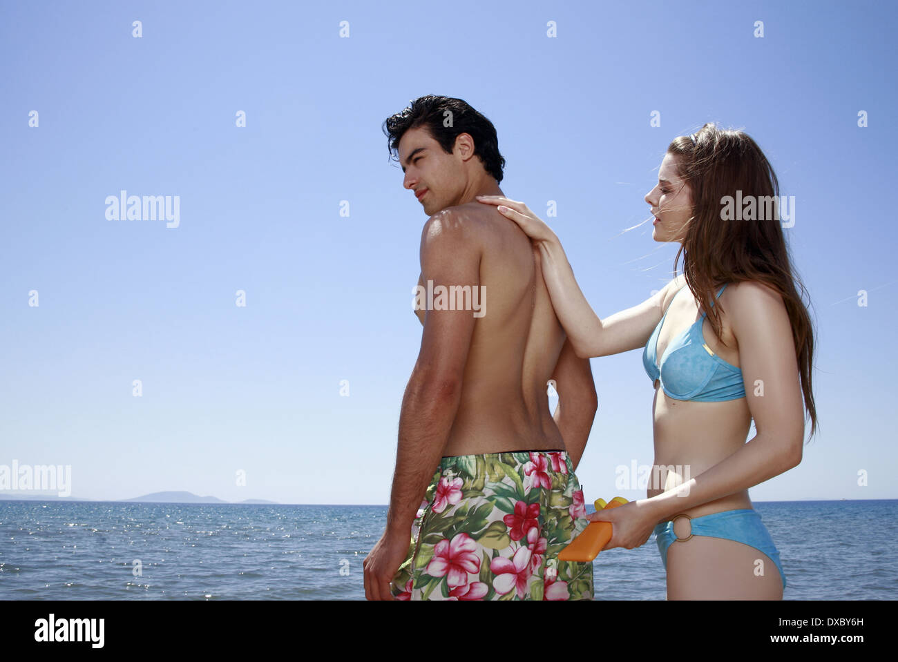 Female young adult applying suntan lotion on male's back Stock Photo