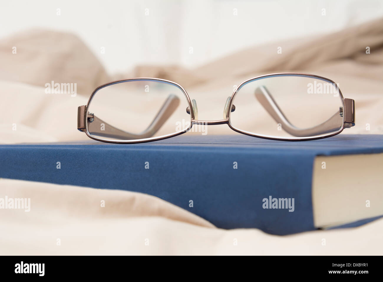 Detail photo showing a pair of glasses and a book sitting on bed Stock Photo