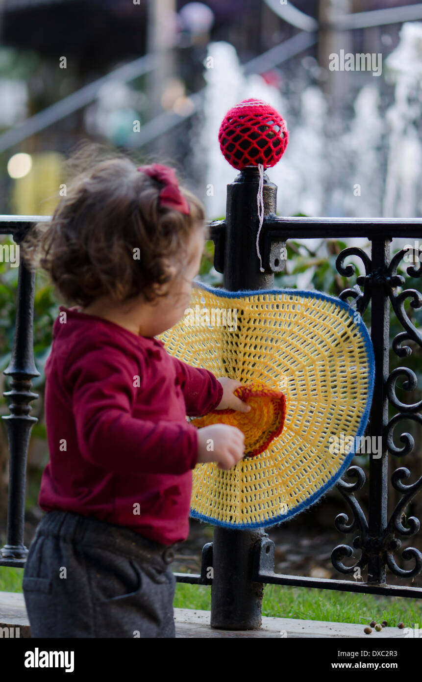 Child playing with knitted circles around a public fence, Yarn bombing, in Fuengirola, Spain Stock Photo