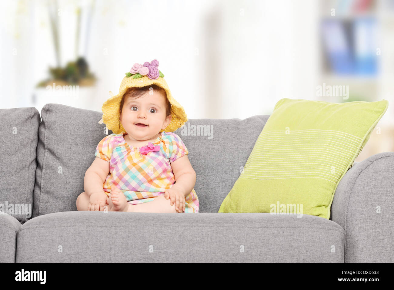 Cute baby girl with a knitted hat sitting on sofa at home Stock Photo