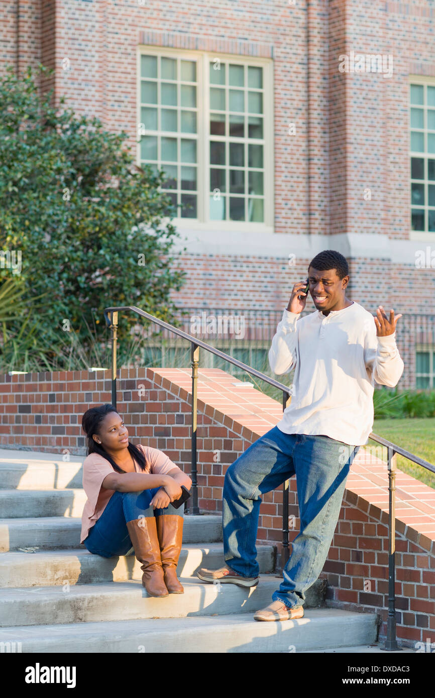 Young man and young woman outdoors on college campus steps, young man using smartphone, Florida, USA Stock Photo