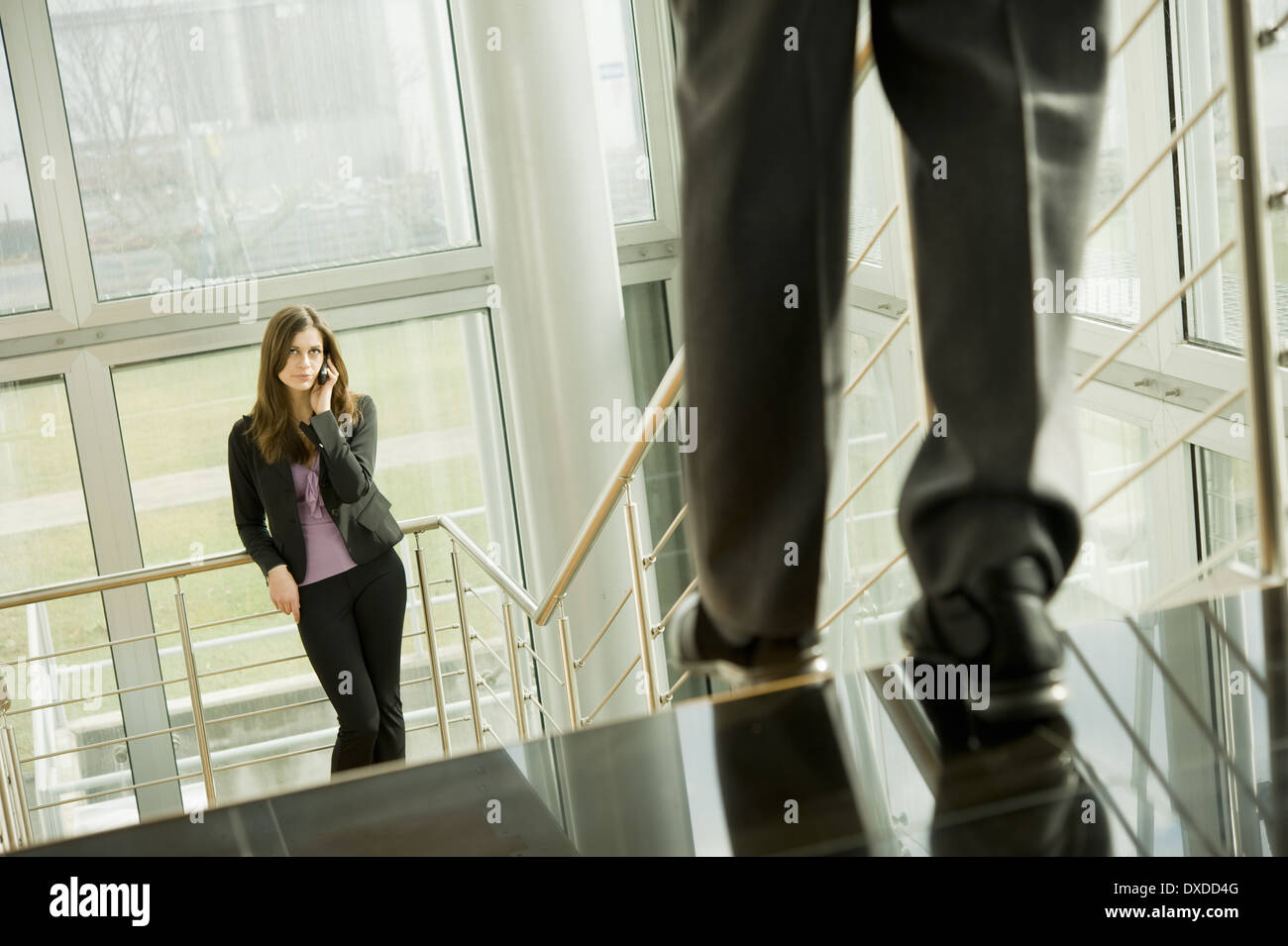 Businesswoman on cell phone and businessman walking down staircase Stock Photo