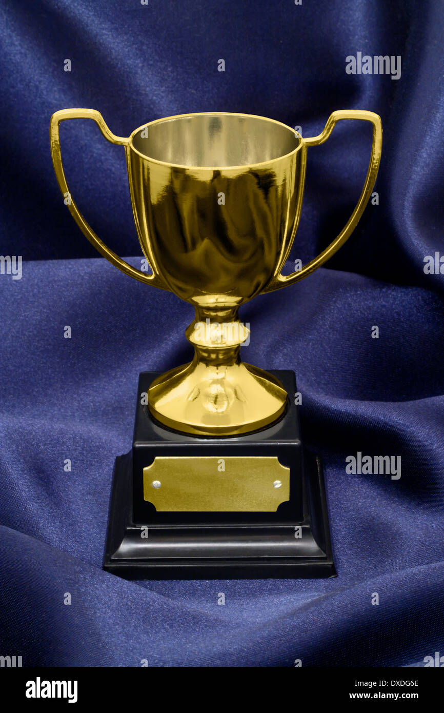 A Gold Winners trophy on a blue silk background great concept for achievement, success or winning a competition or award. Stock Photo