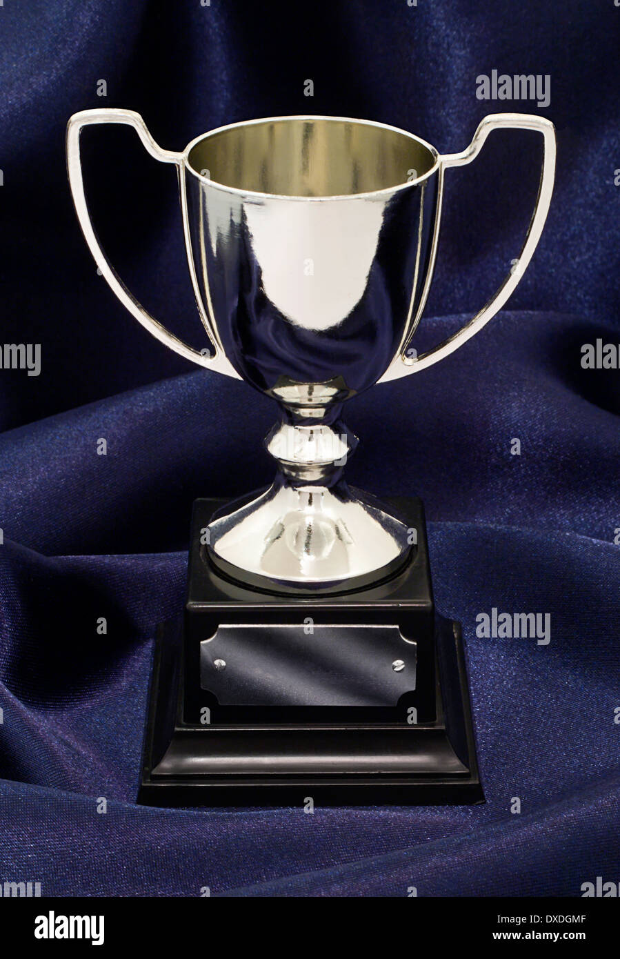 A silver winners trophy on a blue silk background great concept for achievement, success or winning a competition or award. Stock Photo